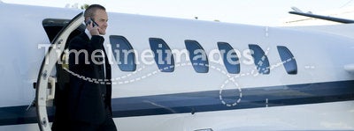 Businessman on cell phone exiting corporate jet