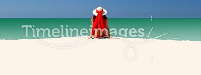 Woman in Red hat and bikini sitting all alone on empty beach