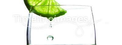 A glass with a piece of lime and drops