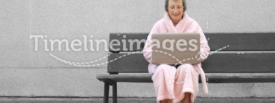 Senior woman in pink robe outdoors with laptop