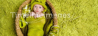 Newborn baby in woolen green hat inside basket