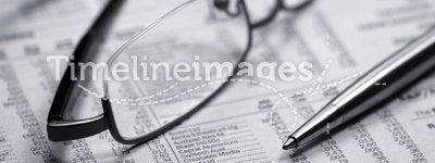 Glasses on a newspaper with a pen