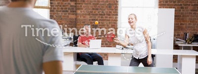 Man and woman in office space playing ping pong