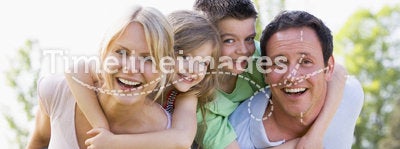 Couple giving two children piggyback rides smiling