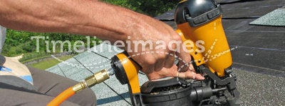 Carpenter uses nail gun to attach asphalt shingles