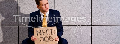 Young businessman squatting with sign Need Job