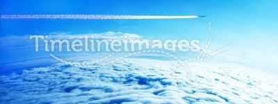 Jet plane contrail in blue sky above the clouds